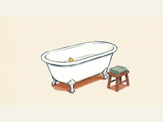 Bañera blanca con un patito de juguete y un taburete de madera con una toalla verde doblada.