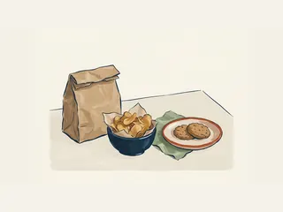 Un cuenco de patatas fritas, un plato con dos galletas y una bolsa de papel sin marca.