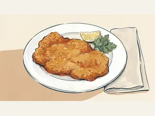 Un filete empanado dorado servido con limón y perejil en un plato de cerámica.