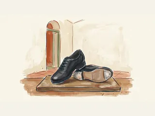 Par de zapatos negros de claqué sobre una tarima de madera; uno muestra las placas metálicas de la suela.