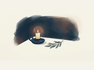 Vela encendida en un portavelas cerámico junto a una rama de olivo.
