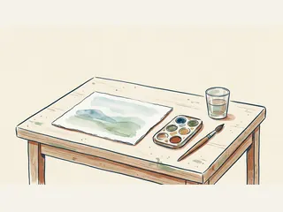 Mesa con un paisaje pintado en acuarela, paleta, pincel y vaso de agua.