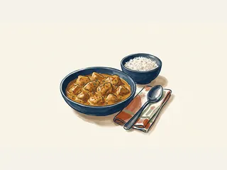 Cuenco de pollo al curry junto a arroz blanco, una cuchara y una servilleta de colores.