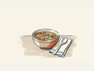 Un cuenco de sopa de verduras junto a una cuchara sobre una servilleta.